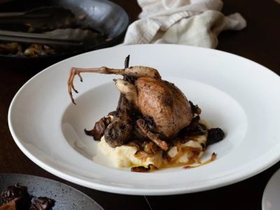 A roast woodcock sitting on a white plate in an elegant restaurant.