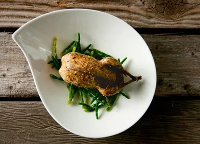 A roast snipe rsting on some samphire on a white plate.