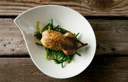 A roast snipe rsting on some samphire on a white plate.